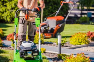 Male Landscaper Doing Garden Maintenance Work with His Professional Equipment Using Two Different Lawn Mowers.