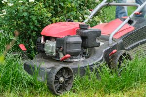 Working lawn mower on green lawn with trimmed grass.